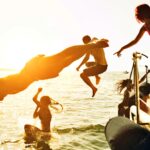 Grupo de amigos saltando al agua desde un yate durante una boat party al atardecer