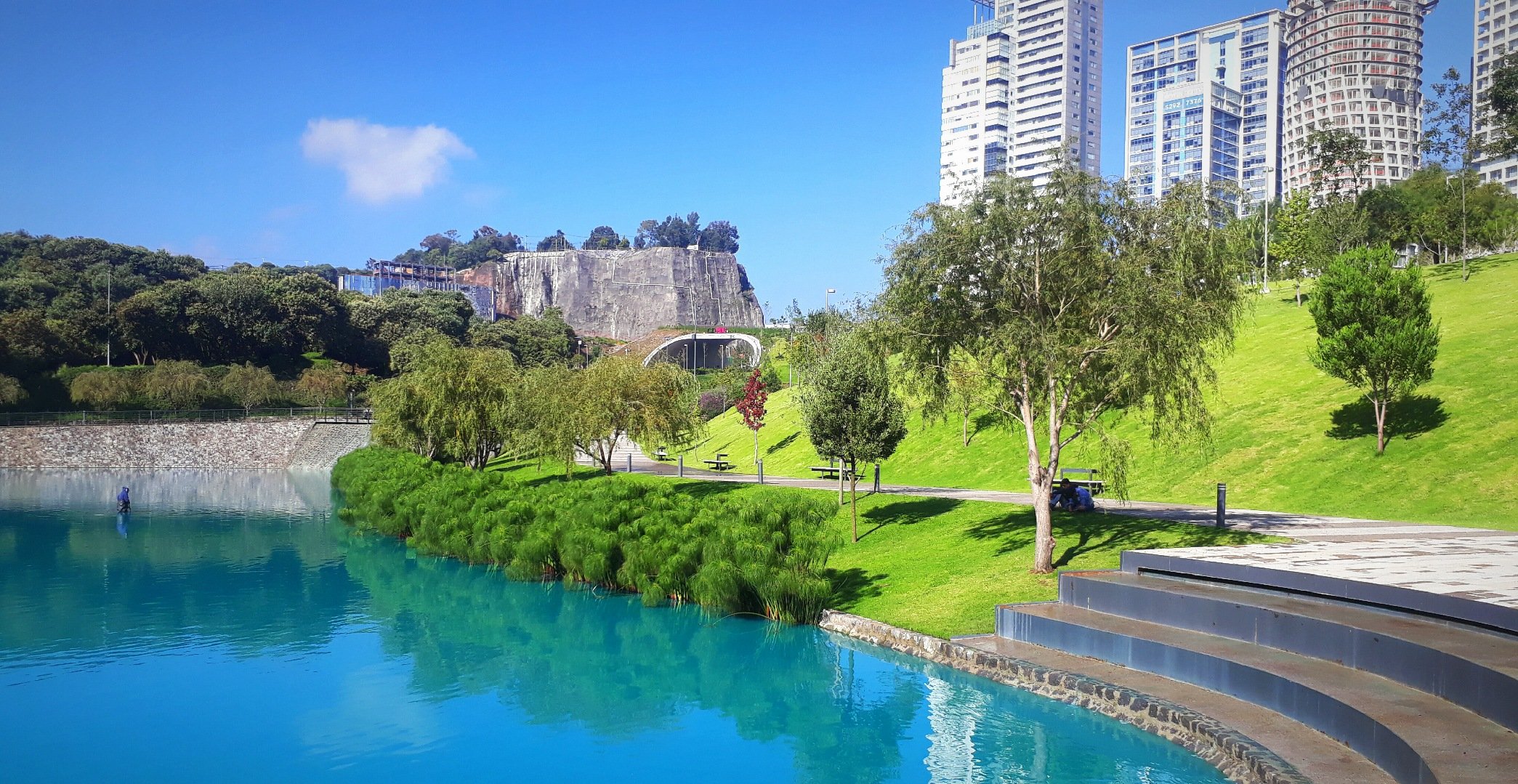 Vista del Parque La Mexicana con su lago artificial, áreas verdes y edificios modernos, accesible por el Tren Interurbano México Toluca.